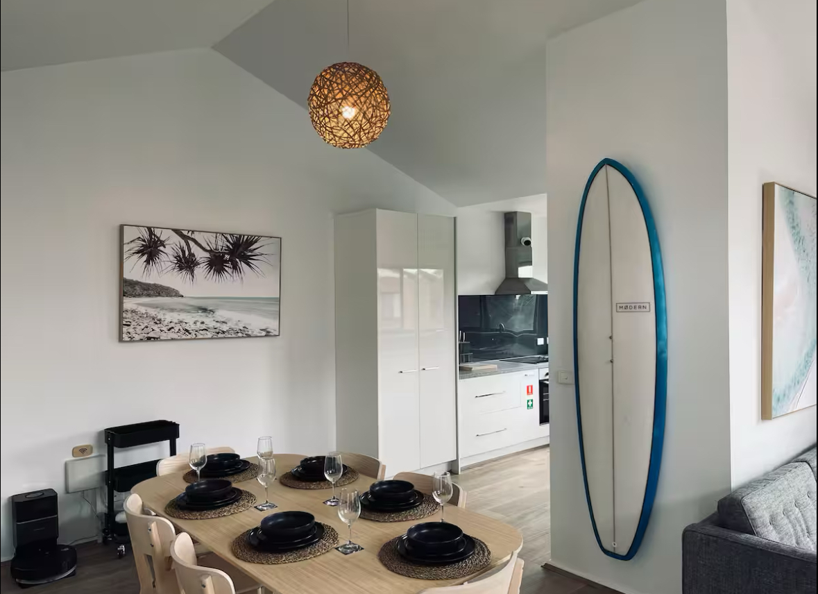 A dining table set for guests beside a surfboard on the wall